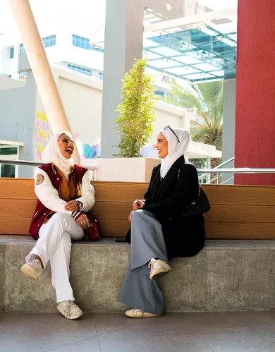 Two AUK students sitting outside on campus, engaging in a thoughtful discussion.