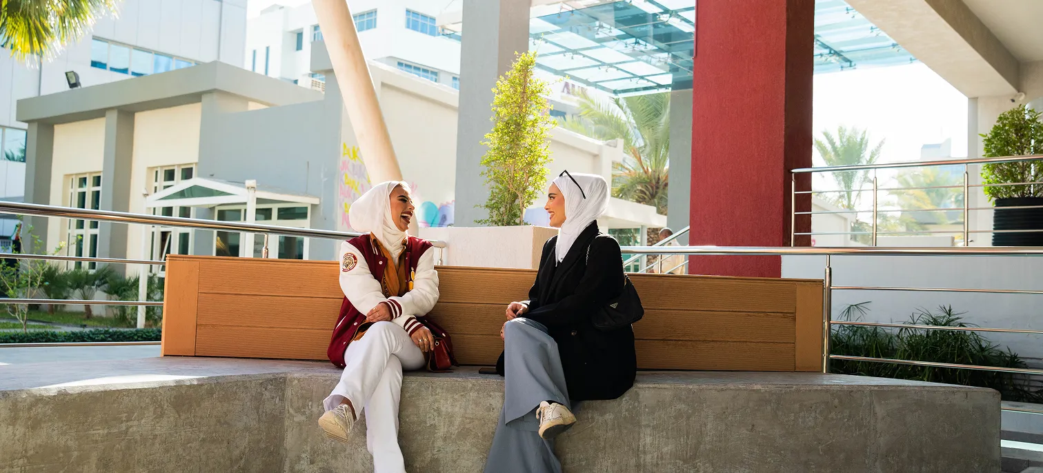 Two AUK students sitting outside on campus, engaging in a thoughtful discussion.