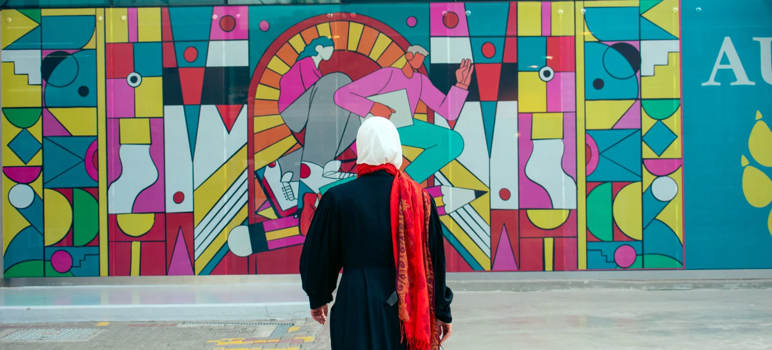 An AUK student admiring the artistic details of a painted wall on campus.