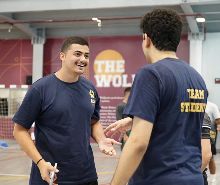 Two AUK students engaged in a discussion on an indoor court.