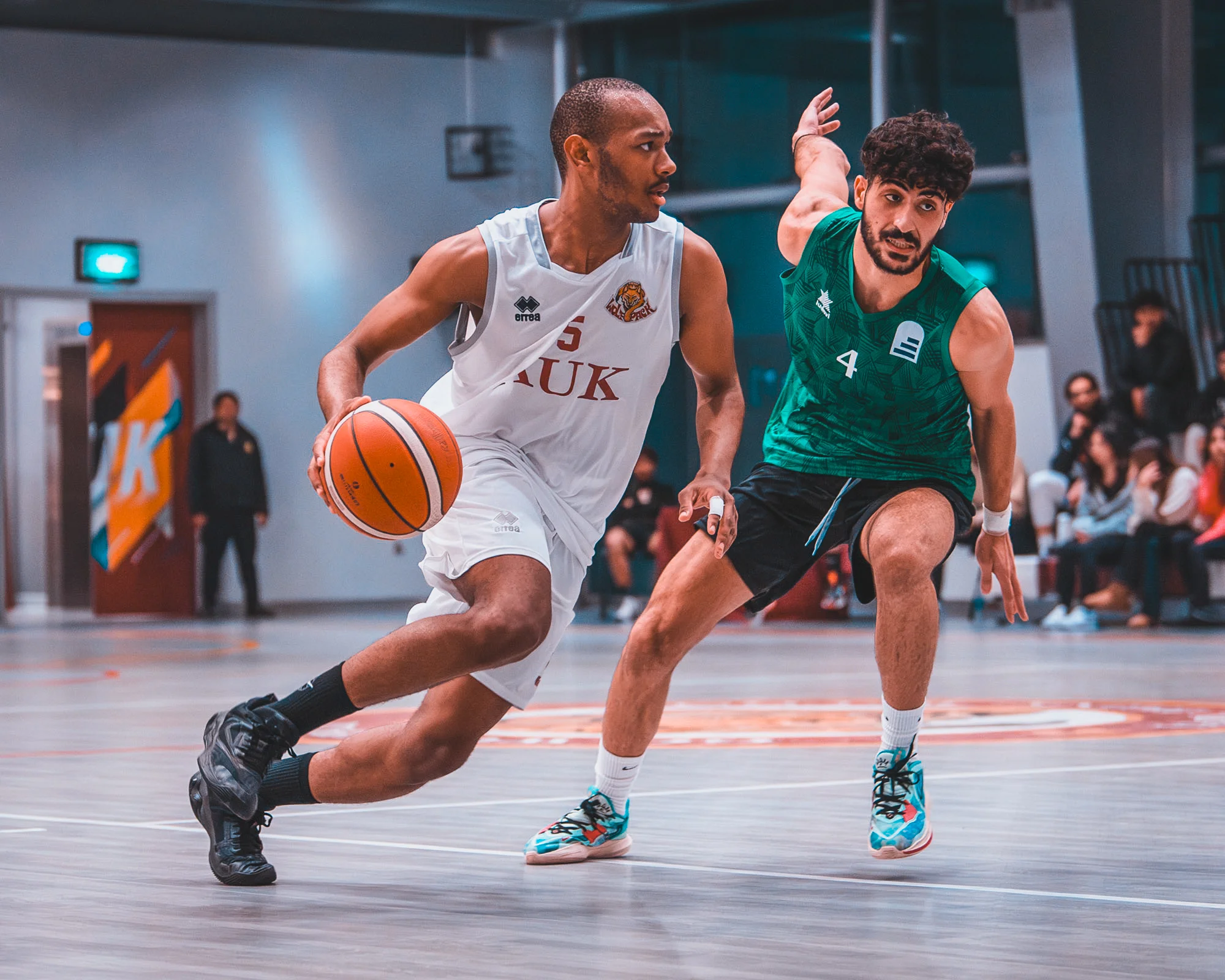Basketball players from AUK and an opposing team competing in an intense match.