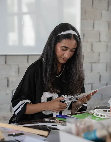 A student cutting a piece of paper with precision for an artwork project at AUK, showcasing her artistic skills and attention to detail.
