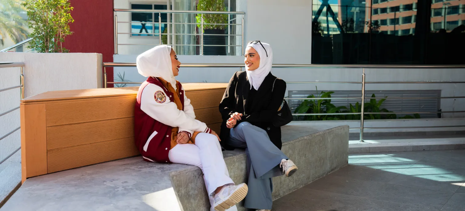 Two AUK students sitting outside on campus, engaging in a thoughtful discussion.
