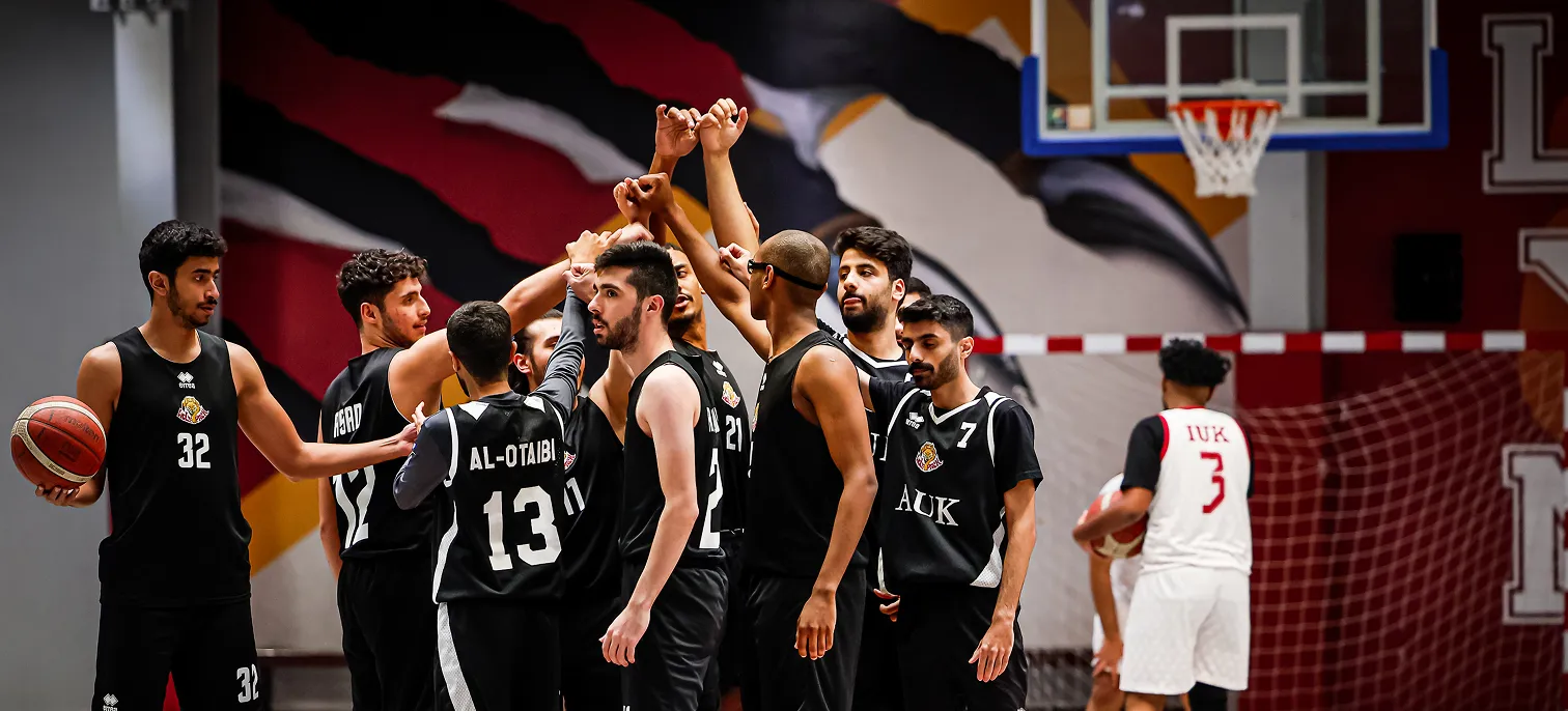 Basketball players at AUK energizing the court, cheering for each other during a spirited game.