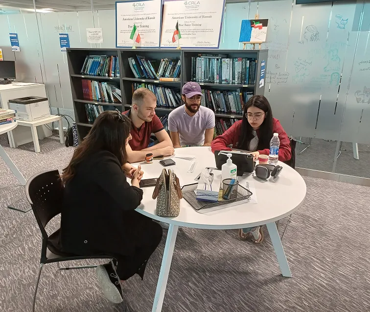 Four AUK students sitting together in the university's library, actively engaged in a discussion about an academic topic.